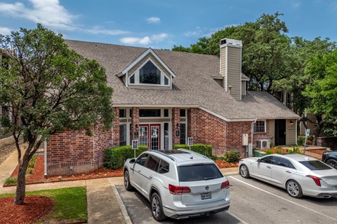 A white car is parked in front of a brick house.