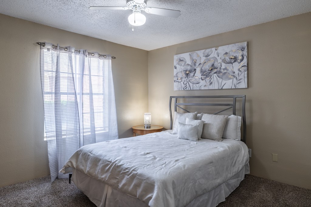 A bedroom with a bed, pillows, a ceiling fan, and a painting on the wall.