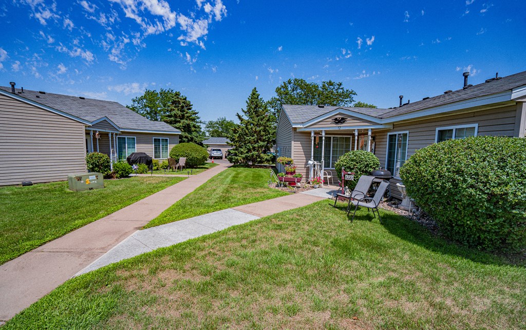 a sidewalk between two houses with a yard and a picnic table