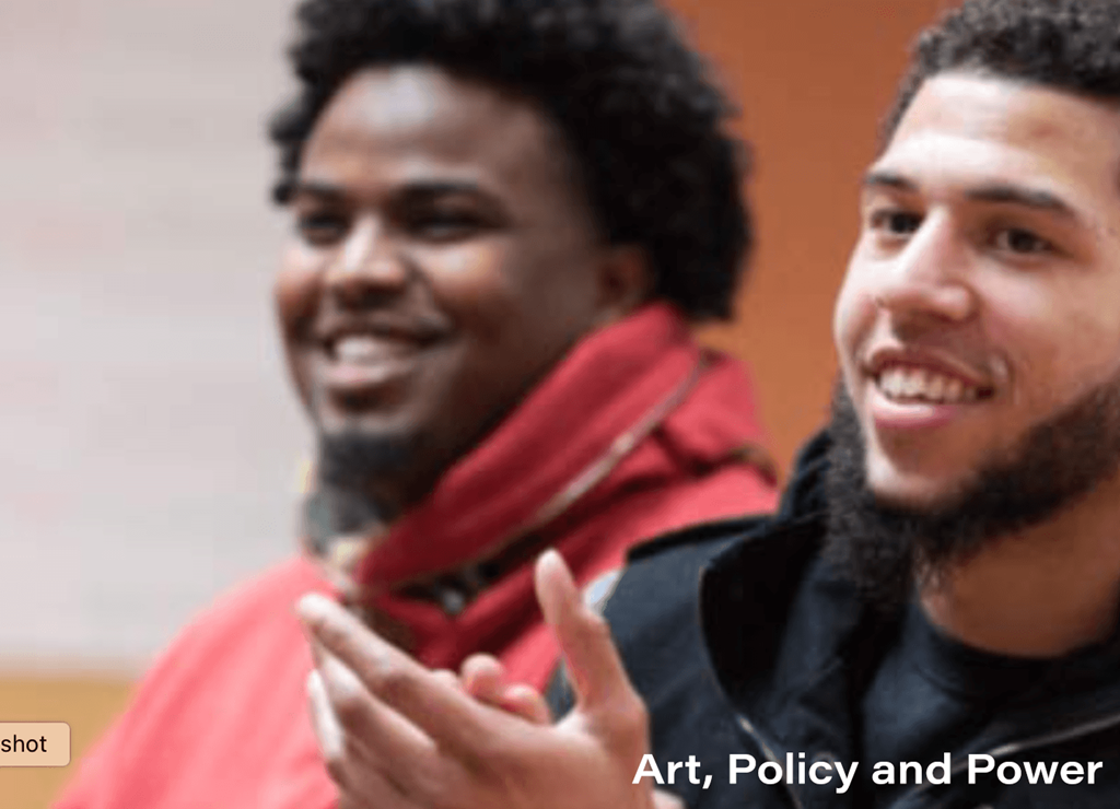 Two men are smiling and one is gesturing with his hand.