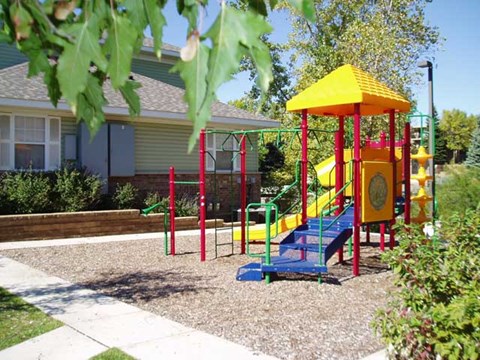 A playground with a yellow and red slide and a red and green swing set.