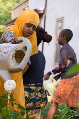 A woman in a yellow garment is pouring water from a white container.
