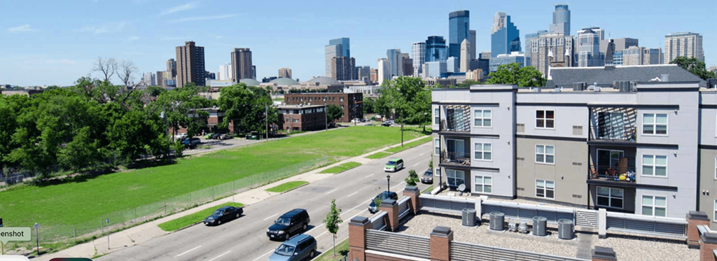 A cityscape with a building in the foreground and a highway in the background.
