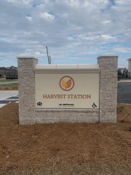 A sign for Harvest Station stands in front of a field.