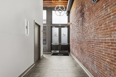A hallway with a brick wall on one side and a glass door on the other.
