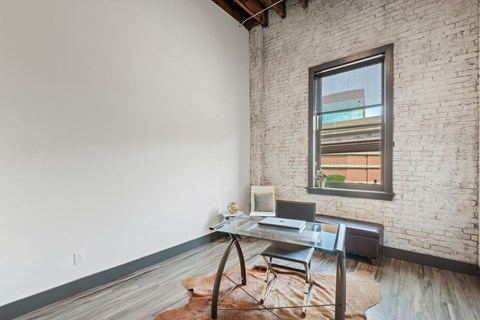 a home office with a glass desk and a brick wall