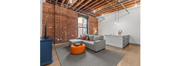 A living room with a grey couch and an orange ottoman.