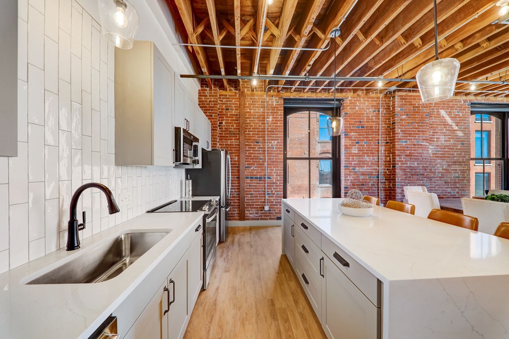 a kitchen with a large white counter top and a exposed brick wall at Greeley Lofts, St. Louis, MO, 63102