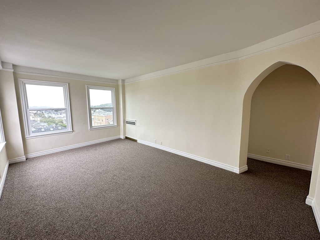 an empty living room with a carpet and two windows