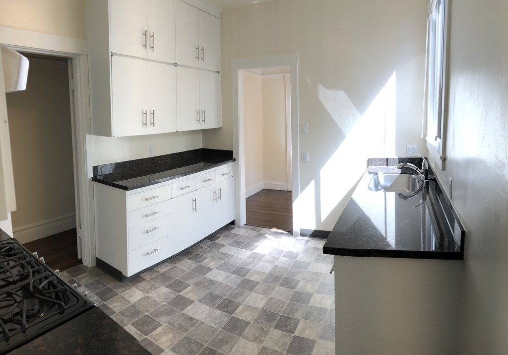 an empty kitchen with white cabinets and black counter tops