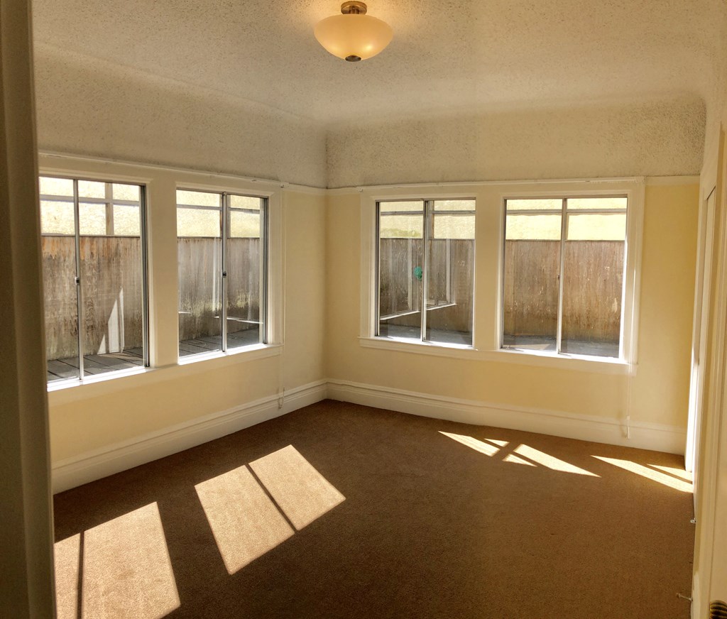 an empty living room with three windows and a carpet