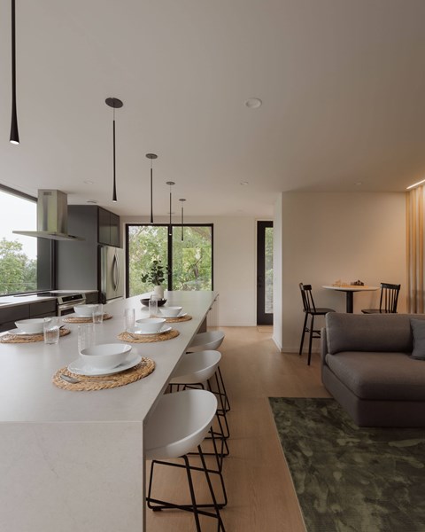 A modern kitchen with a long white counter and chairs.