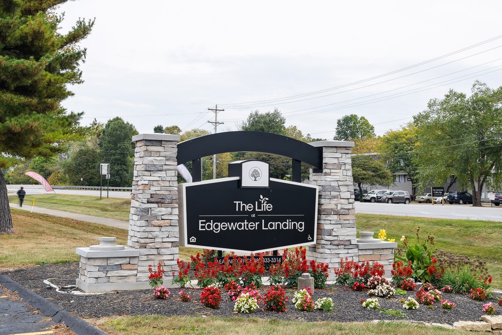 A sign that says The Life Edgewater Landing is surrounded by flowers.