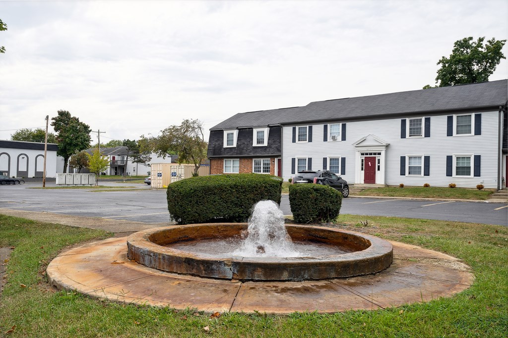 A fountain in the middle of a grassy area in front of a building.