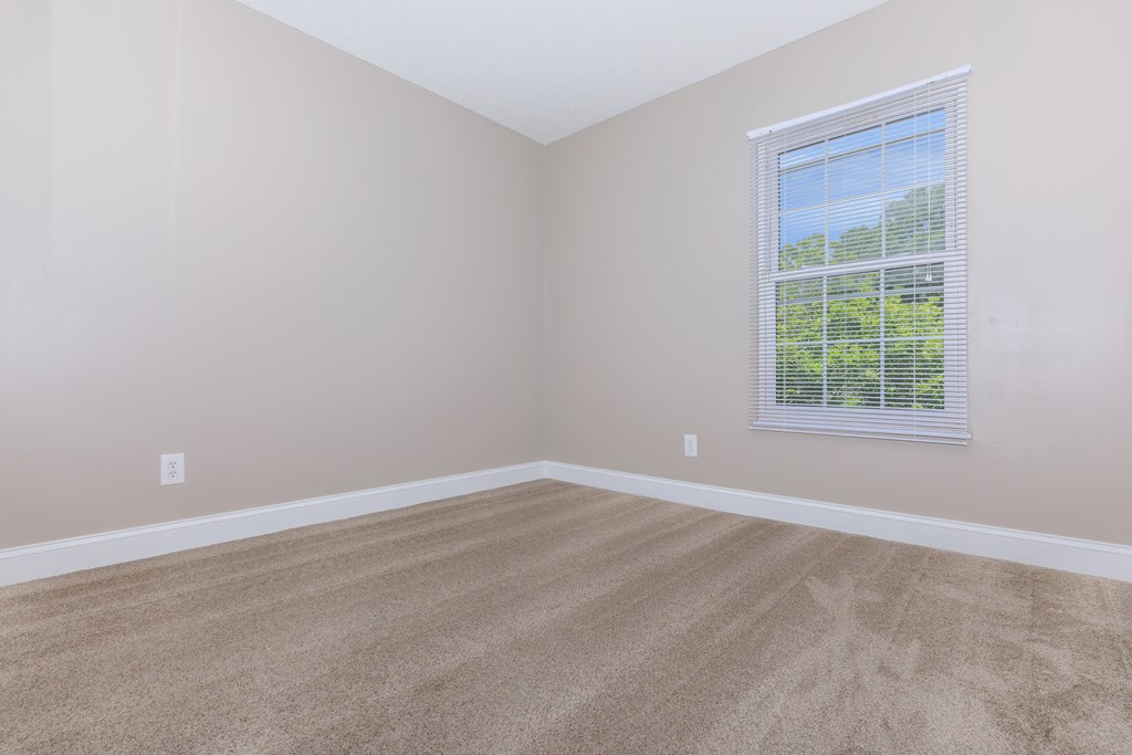 a bedroom with beige carpet and a large window