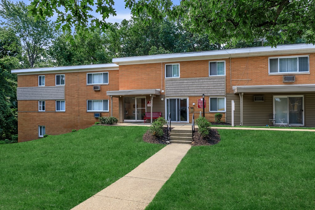 a brick building with a green lawn and trees in the background