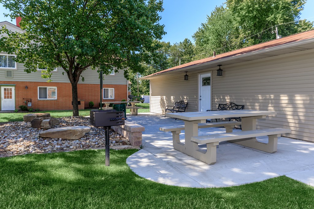a patio with a picnic table and grill in front of a house