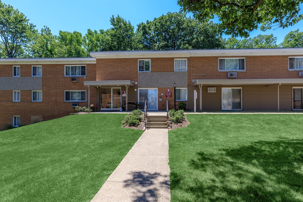a brick apartment building with a green lawn and trees in the background