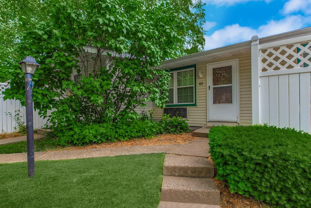 a small house with a white fence and a tree in front of it