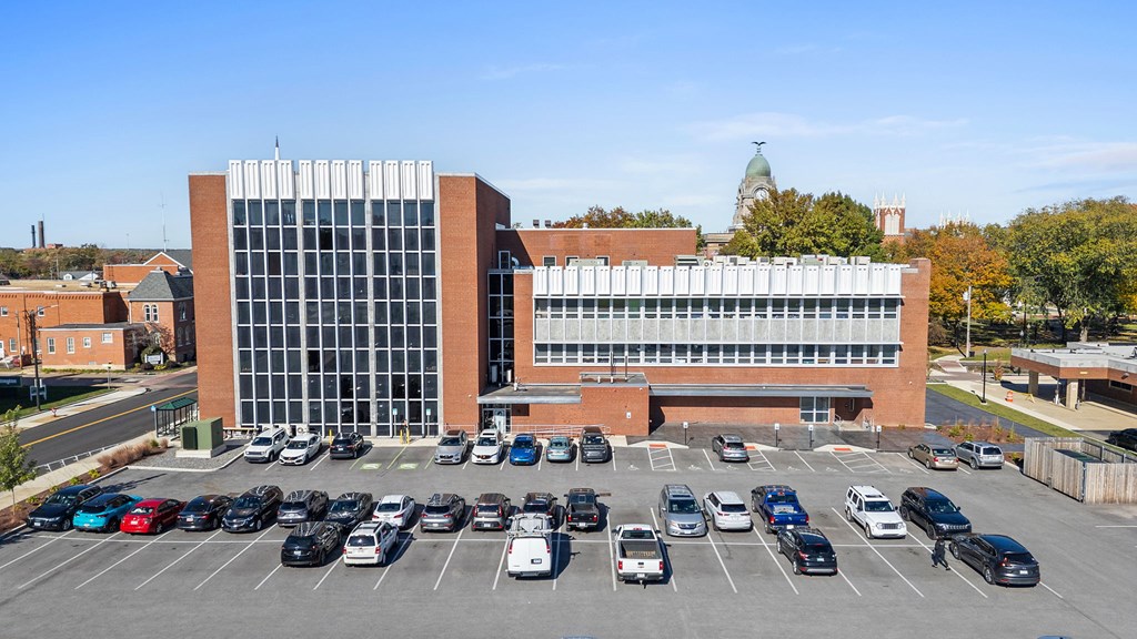 A parking lot in front of a large building with a glass facade.