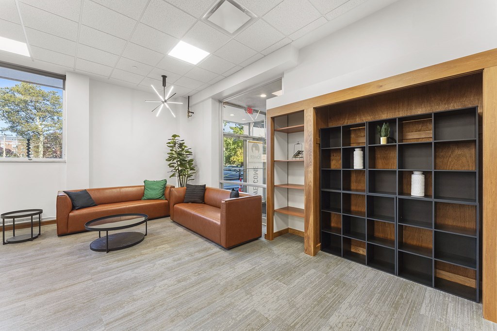 A room with a brown leather couch, a black coffee table, and a wooden bookshelf.