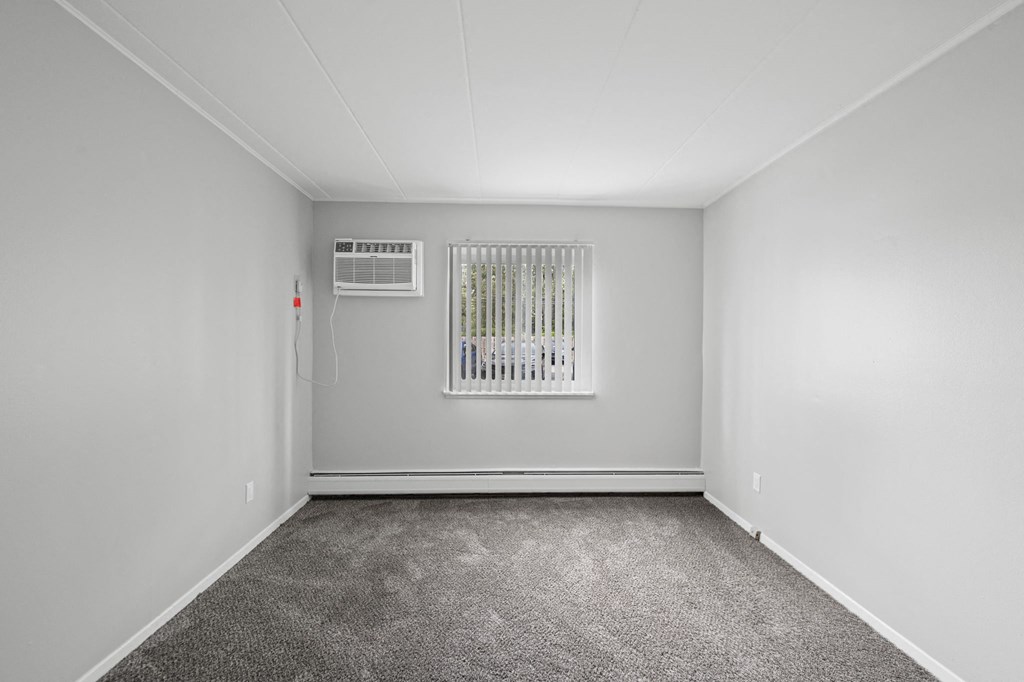 a room with white walls and carpet and a heater on the wall