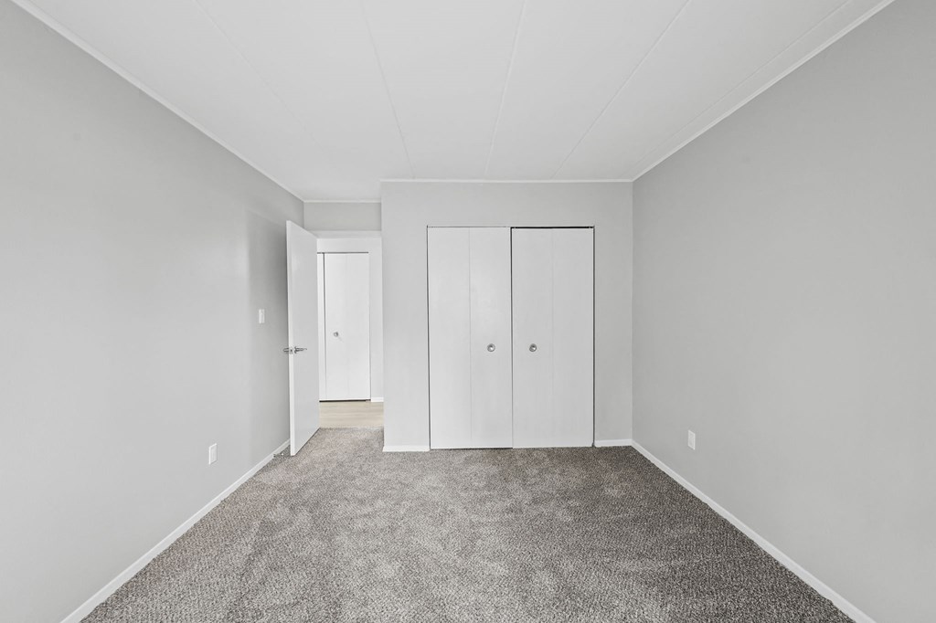 a bedroom with white walls and carpet and white closets