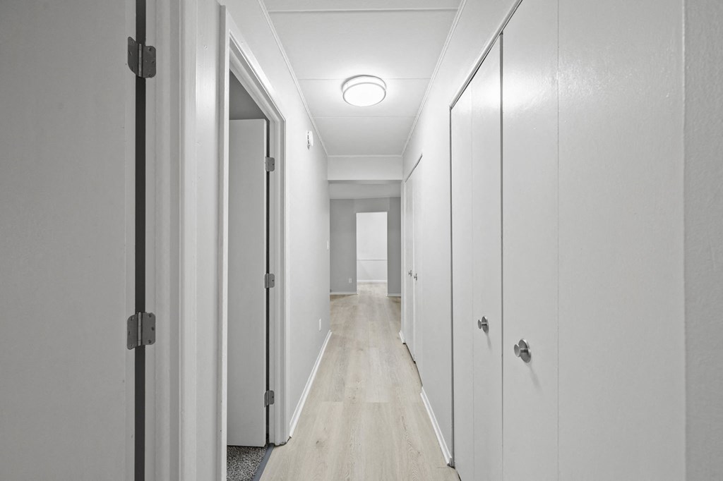a long white hallway with white doors and white walls and a white wood floor with