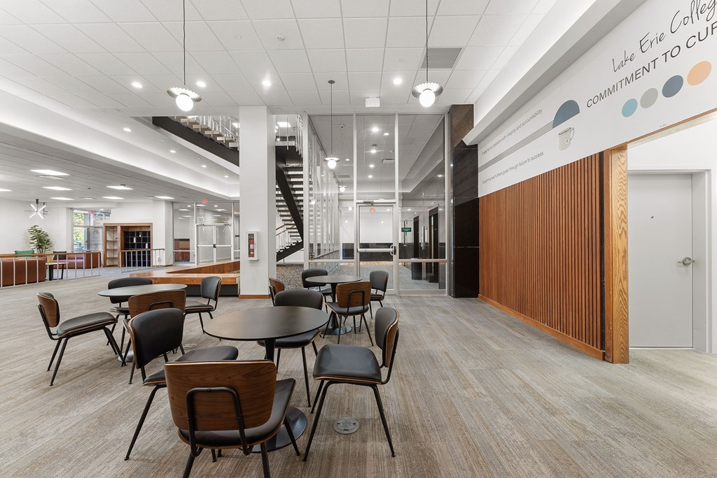 A modern interior of Lake Erie College with a staircase and a long table with chairs.