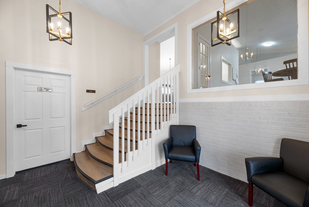 A hallway with a staircase, a chair, and a mirror.