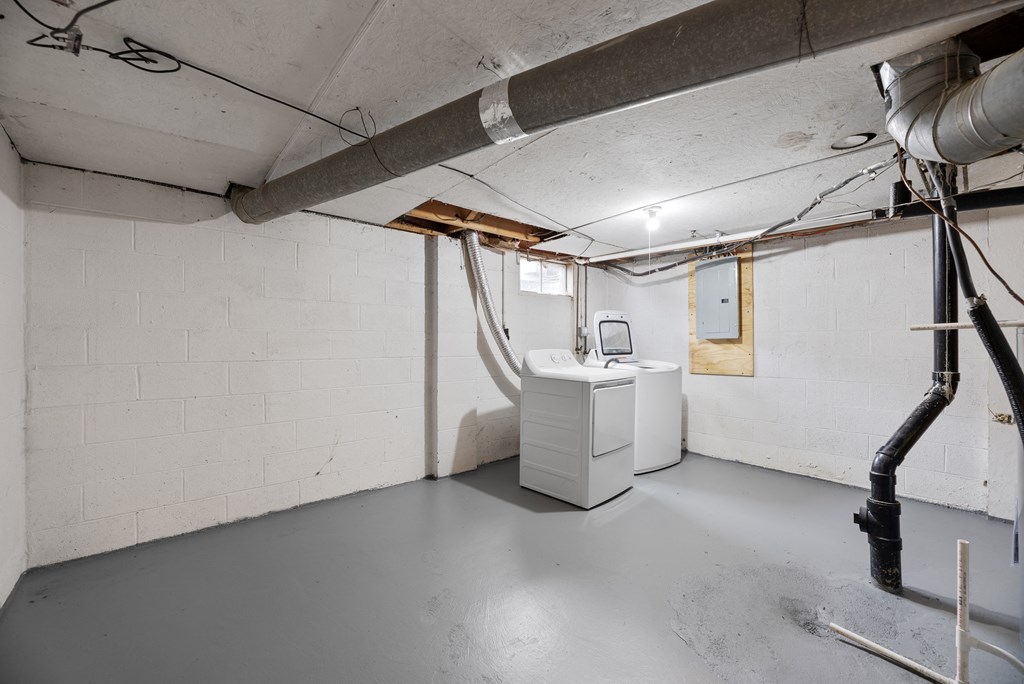 A room with white walls and a concrete floor with a white cabinet and a pipe running along the wall.