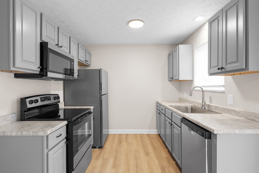 A kitchen with a refrigerator, oven, microwave, and sink.