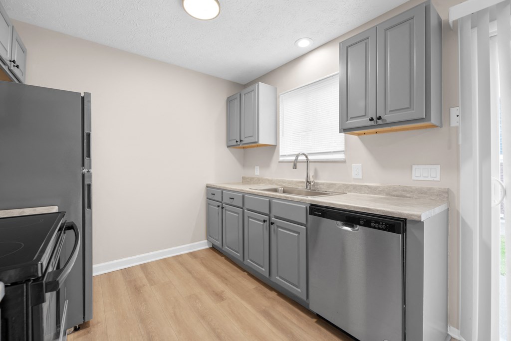 A kitchen with a black refrigerator and grey cabinets.
