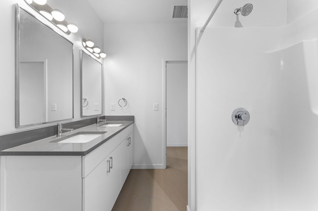 A white bathroom with a sink, mirrors, and a shower.