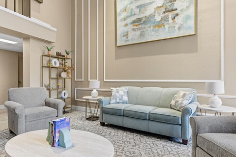 A living room with a grey couch, a grey armchair, a white coffee table, and a large abstract painting on the wall.