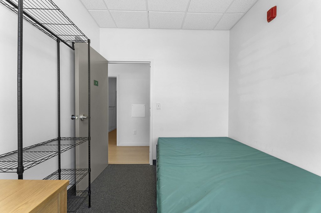 A room with a bed, a desk, and a metal shelving unit.