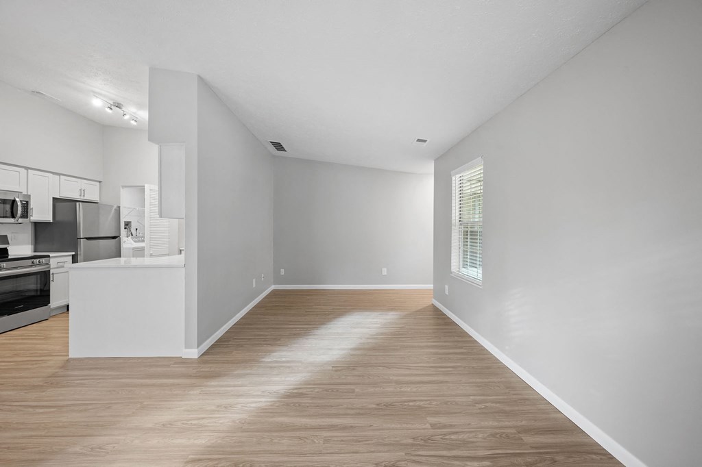 a living room and kitchen with white walls and wood floors
