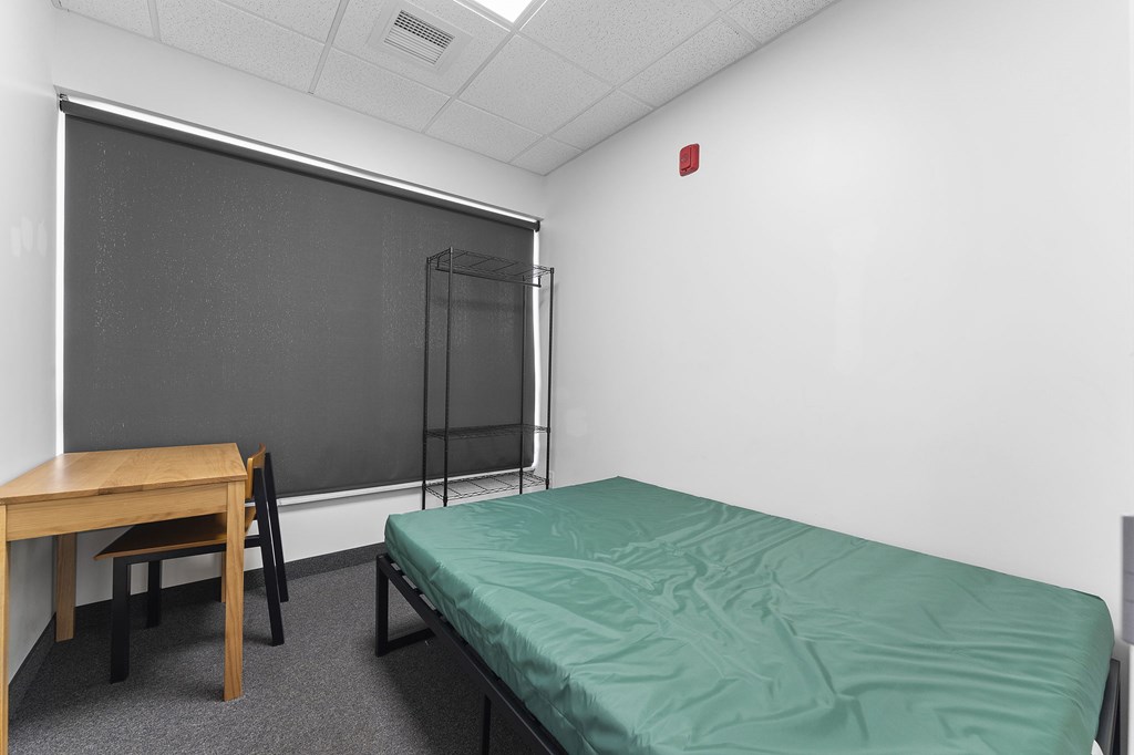A room with a bed, desk, chair, and a blackboard.