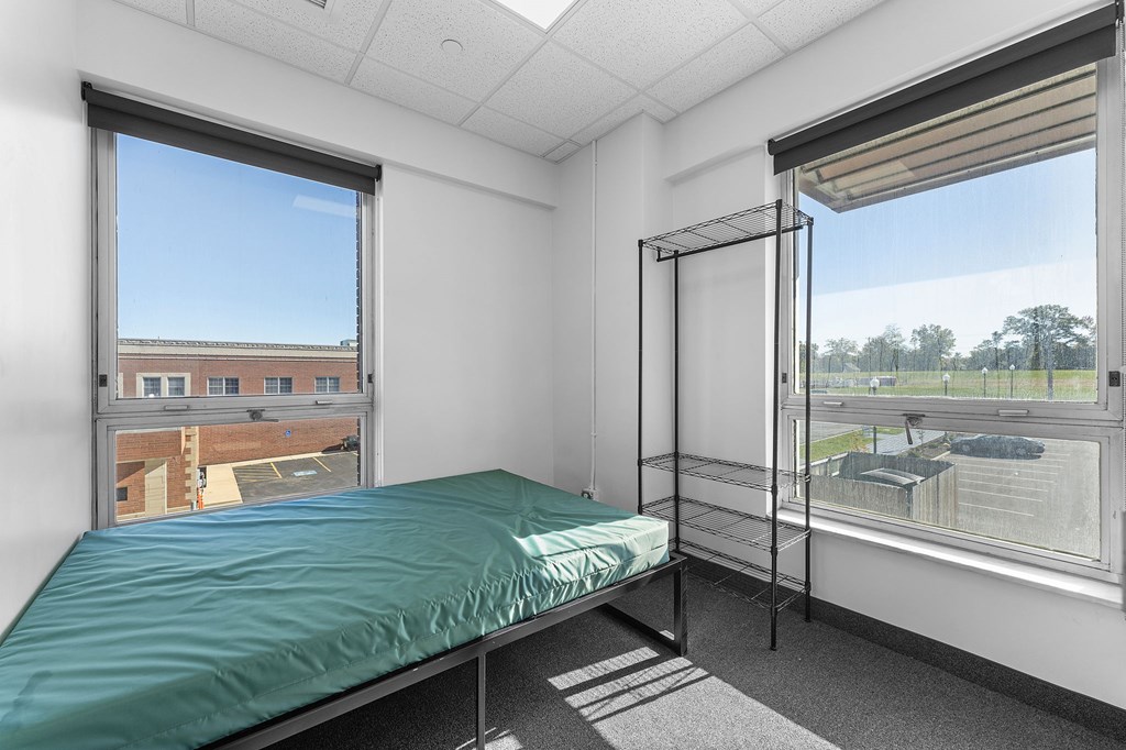 A bedroom with a bed, a window with a view of a building and trees, and a hanging clothes rack.