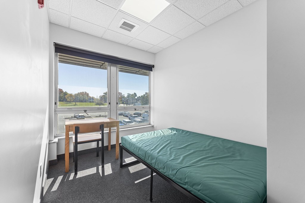 A room with a bed, table and chairs with a window overlooking a parking lot.