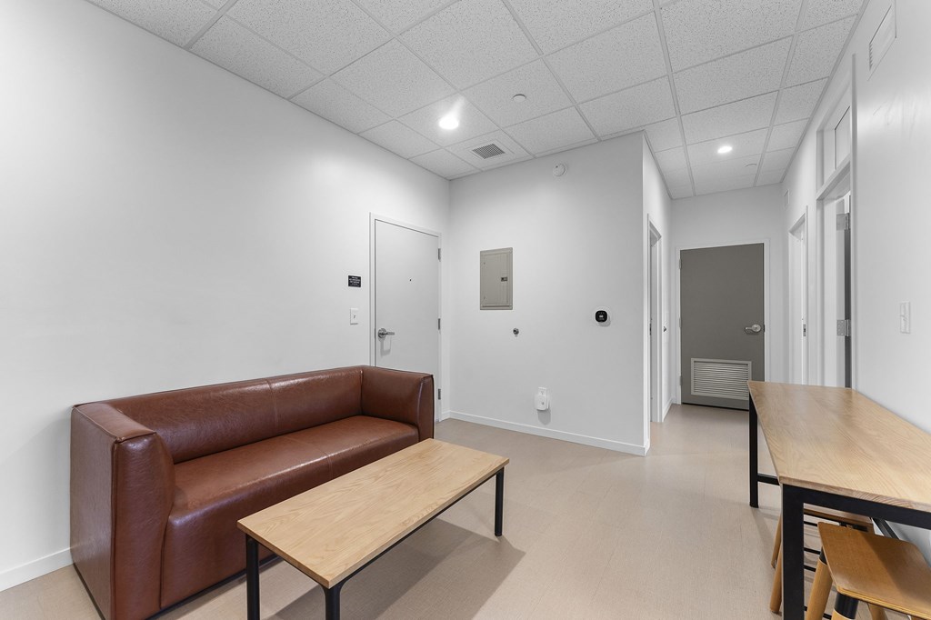 A brown leather couch sits in a white room with a wooden table in front of it.