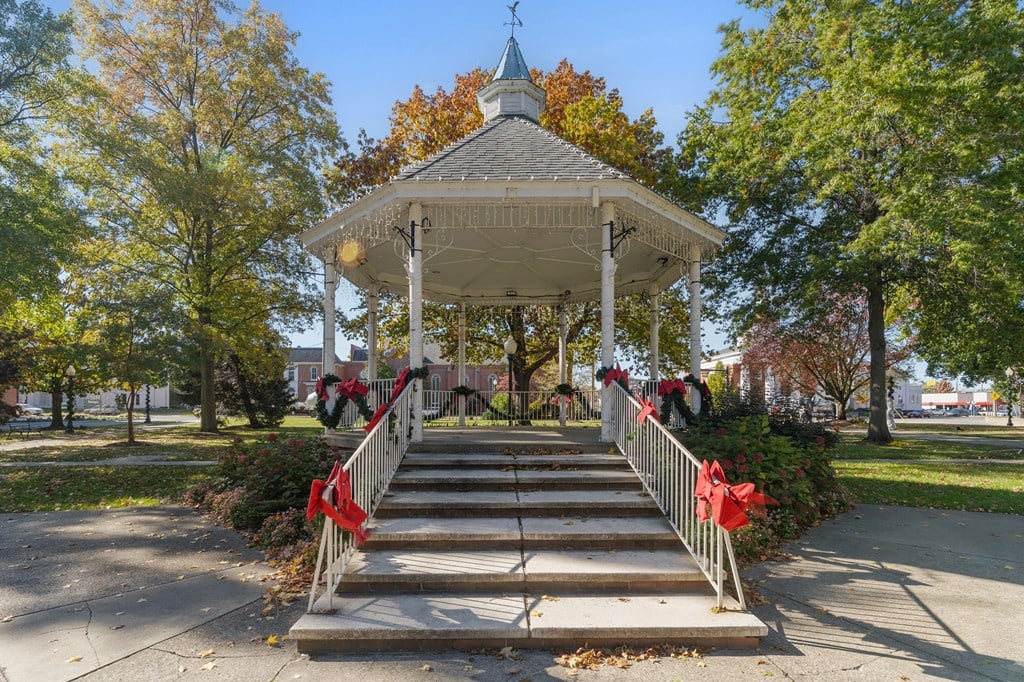 A gazebo with a red bow is surrounded by trees.