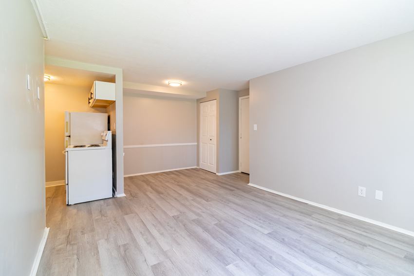an empty living room with a refrigerator and a kitchen
