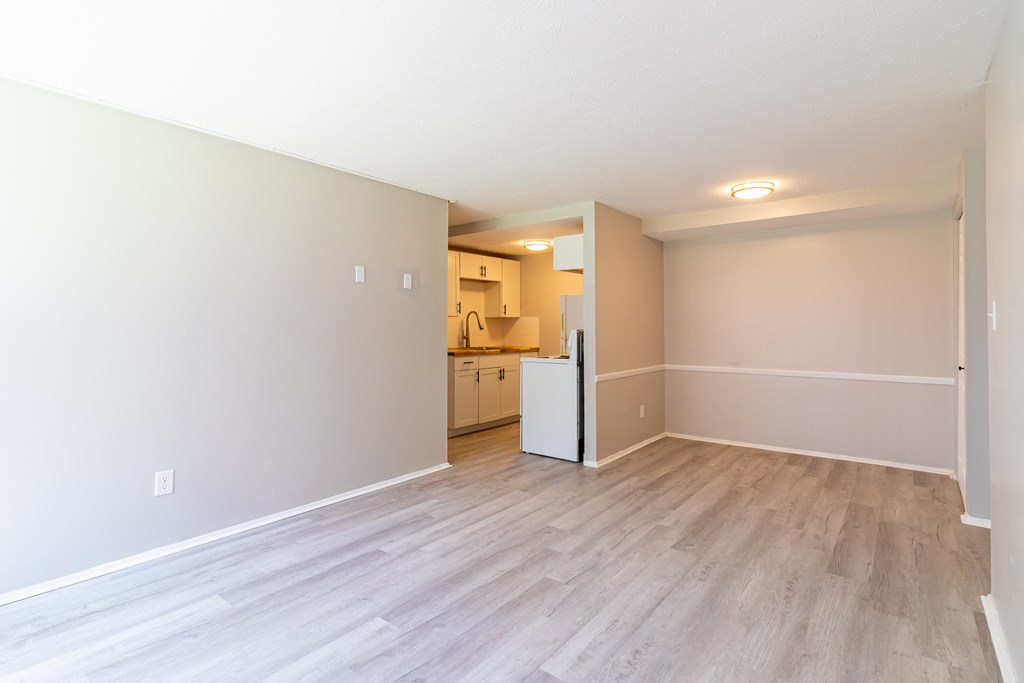 an empty living room and kitchen with wood flooring and white walls