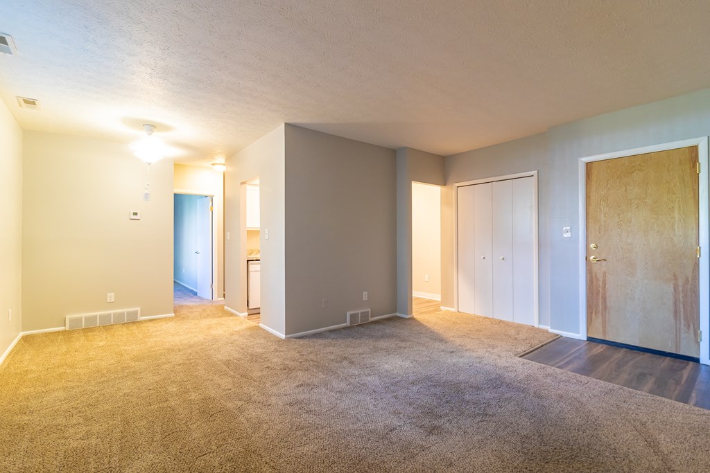 an empty living room with carpet and a door to a bedroom