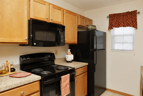 A black refrigerator sits in a kitchen with wooden cabinets.at Abbie Cove, Canal Winchester, OH, 43110