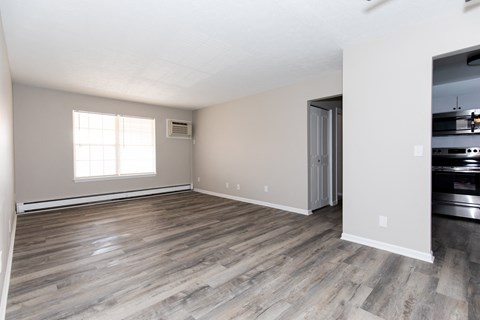 an empty living room with wood flooring and a kitchen