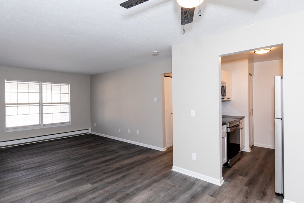 an empty living room with wood flooring and a kitchen