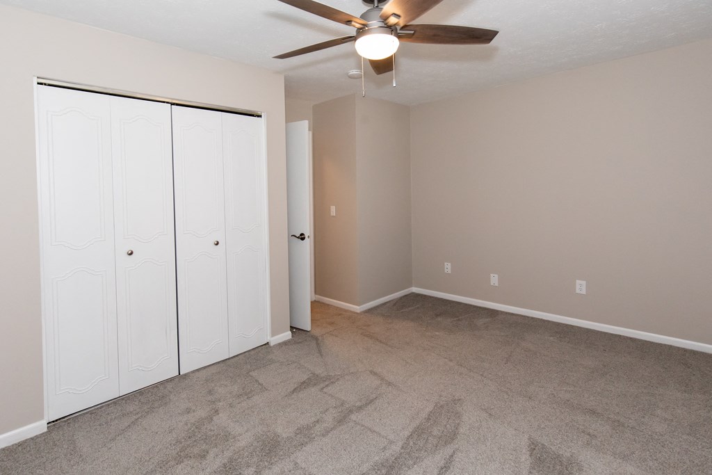 an empty living room with a ceiling fan and two closets