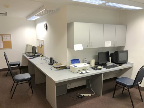 A room with a desk, chairs, and computers.